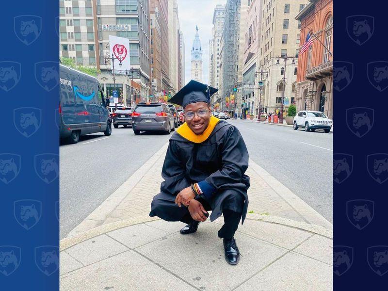 Man in cap and gown crouching near City Hall in Philadelphia